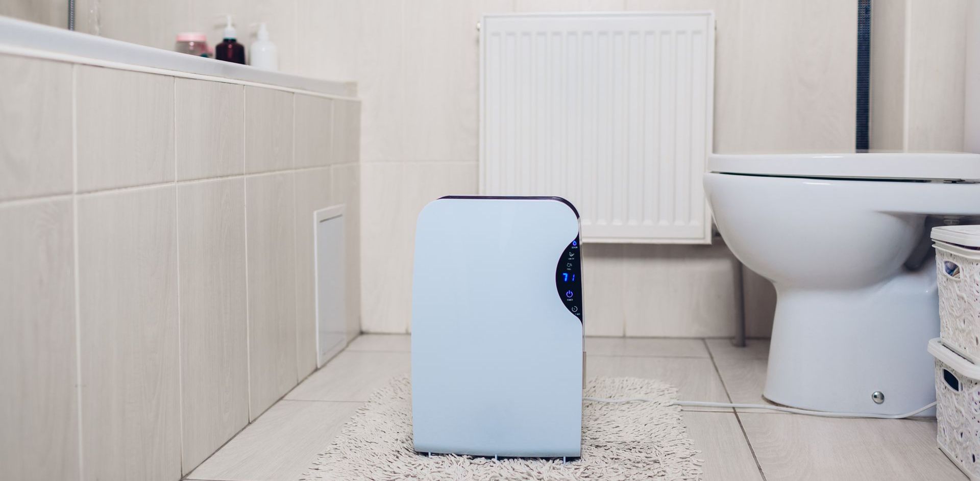 A blue air purifier is sitting on the floor in a bathroom next to a toilet.