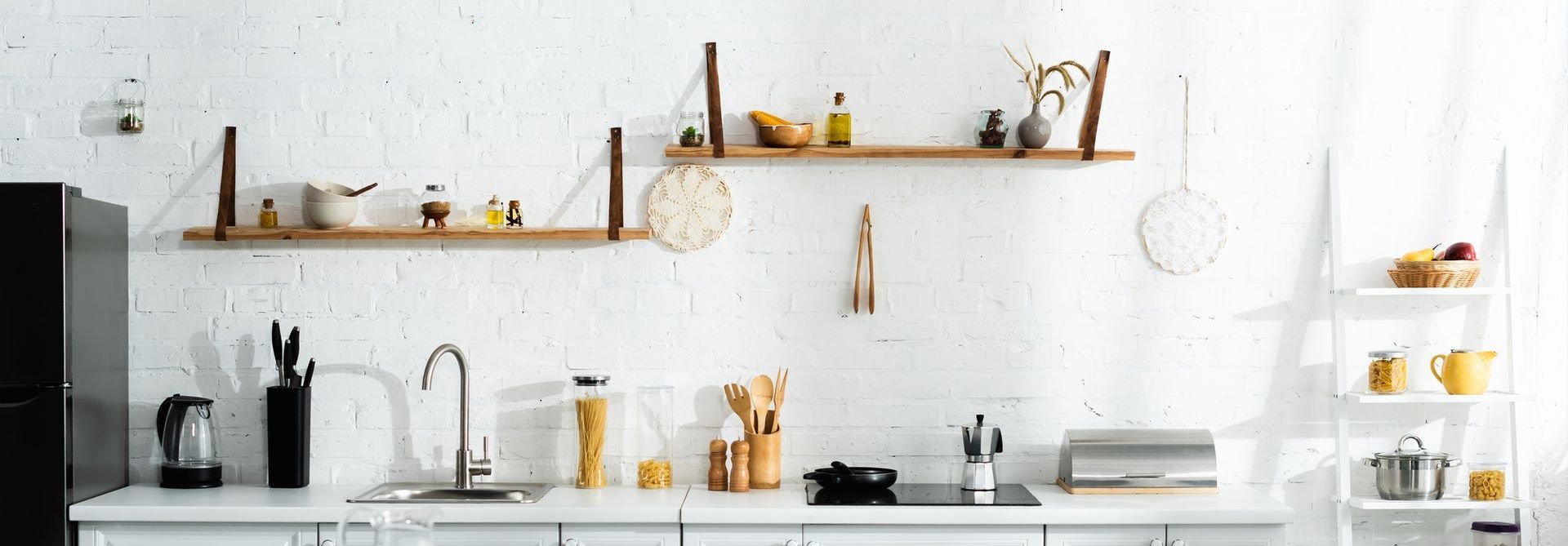 A kitchen with a sink , stove , refrigerator and shelves.