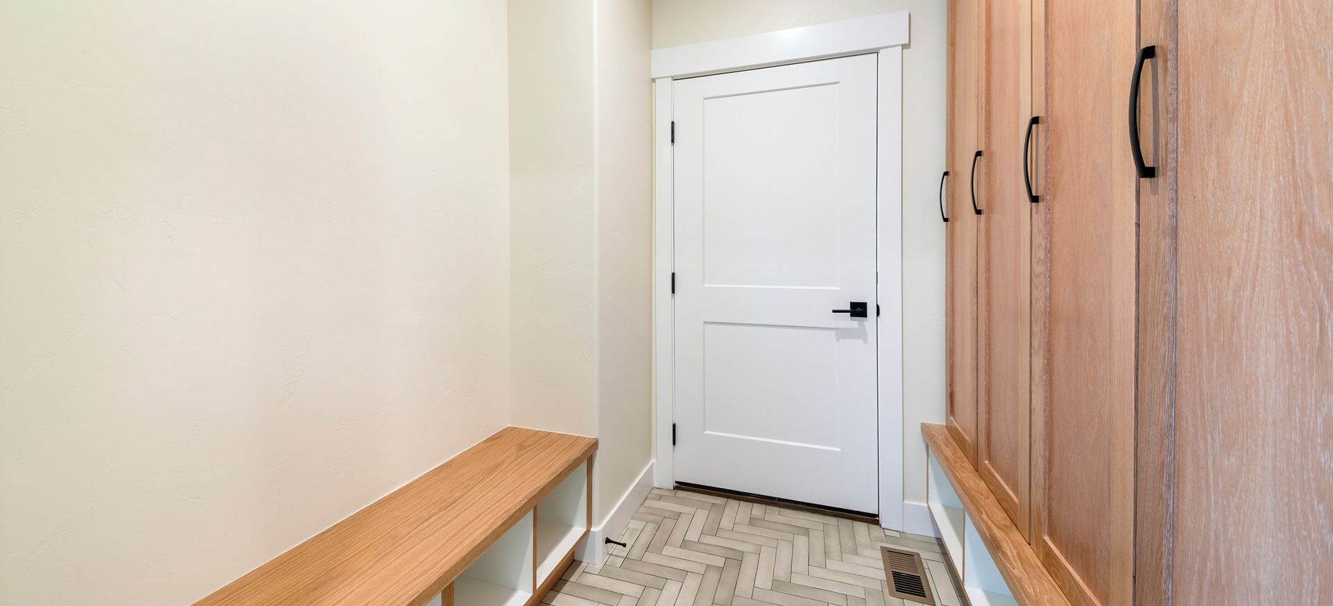 A hallway with a wooden bench and cabinets leading to a door.