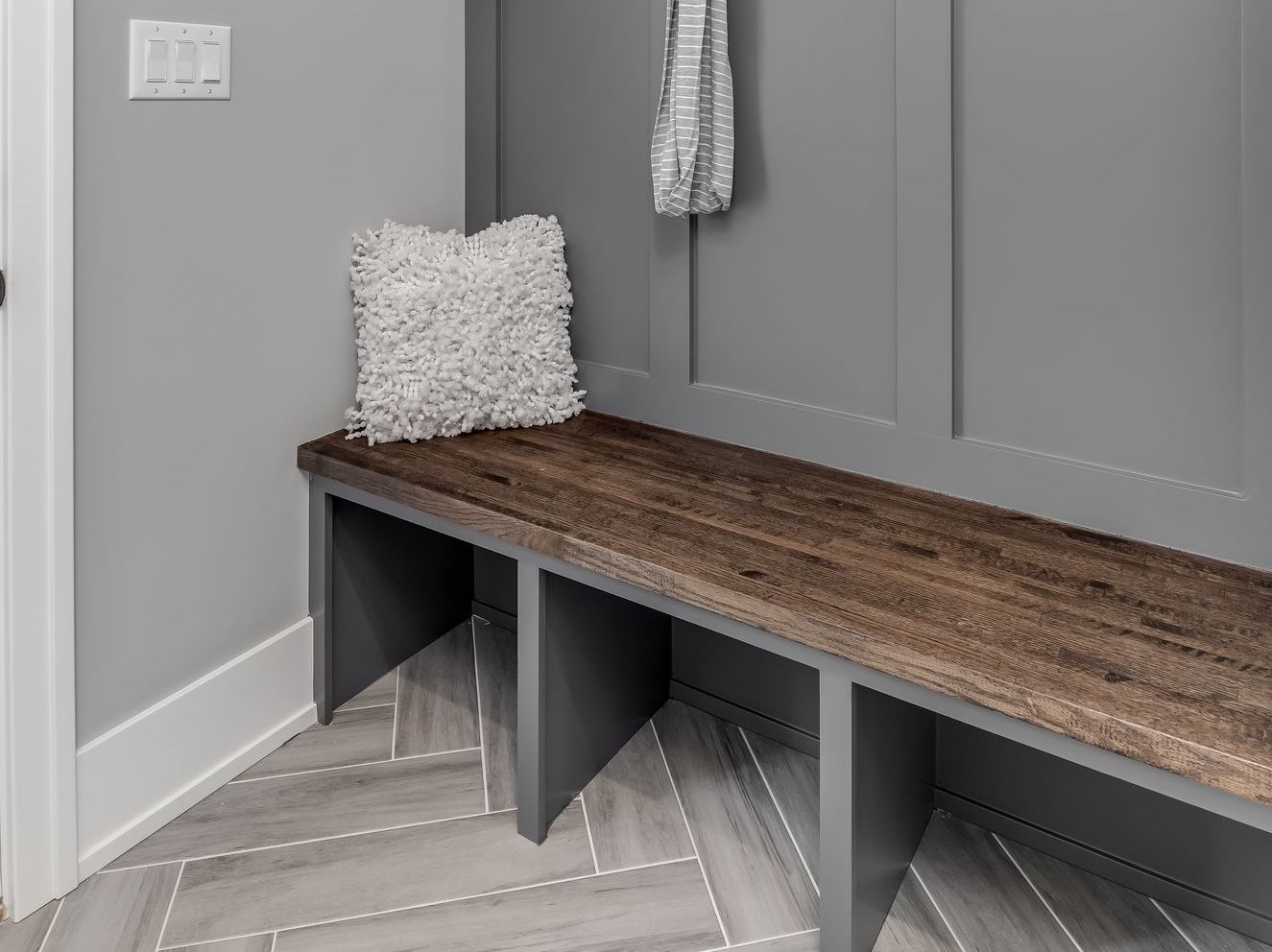 A wooden bench in a mud room with a pillow on it.