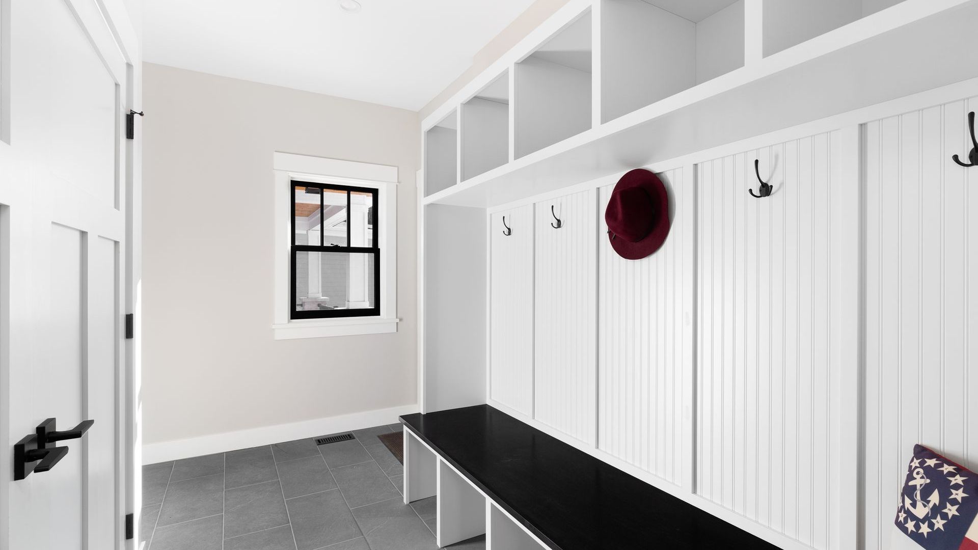 A mud room with a bench , hooks , shelves and a window.