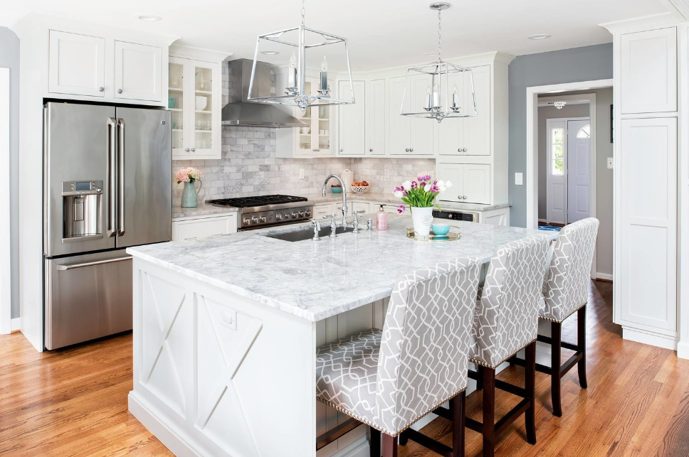 A kitchen with white cabinets , marble counter tops , stainless steel appliances and a large island.