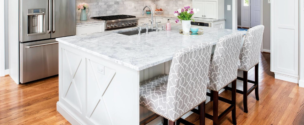 A kitchen with a large island , stools and a refrigerator.