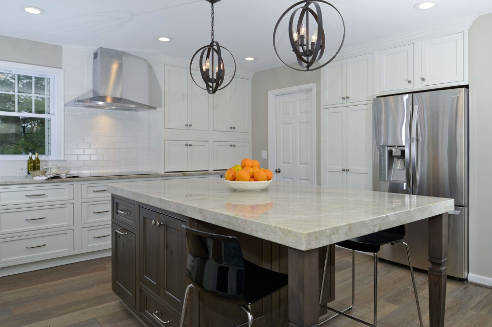 A kitchen with a large island , stainless steel appliances , white cabinets and a bowl of oranges on the counter.