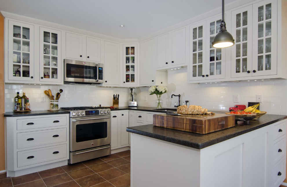 A kitchen with white cabinets , stainless steel appliances , and a wooden cutting board on the counter.