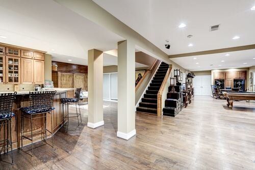 A large basement with hardwood floors , a pool table and stairs.