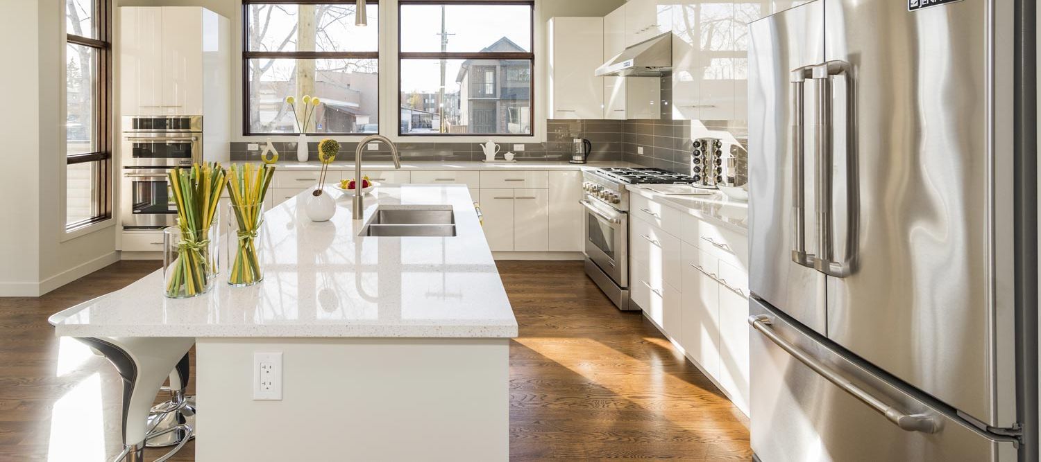 A kitchen with white cabinets , stainless steel appliances , a refrigerator and a sink.