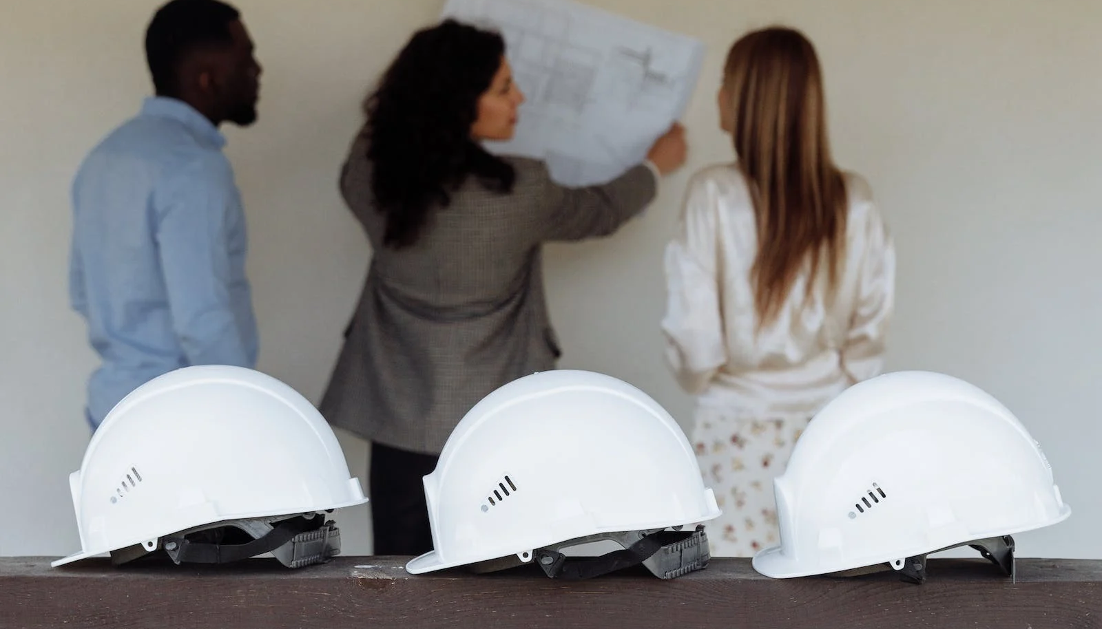 A group of people are standing around a table with hard hats and looking at a blueprint.