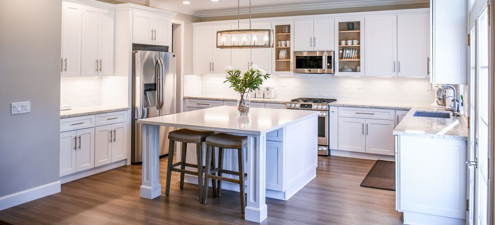 A kitchen with white cabinets and stools and a large island in the middle.
