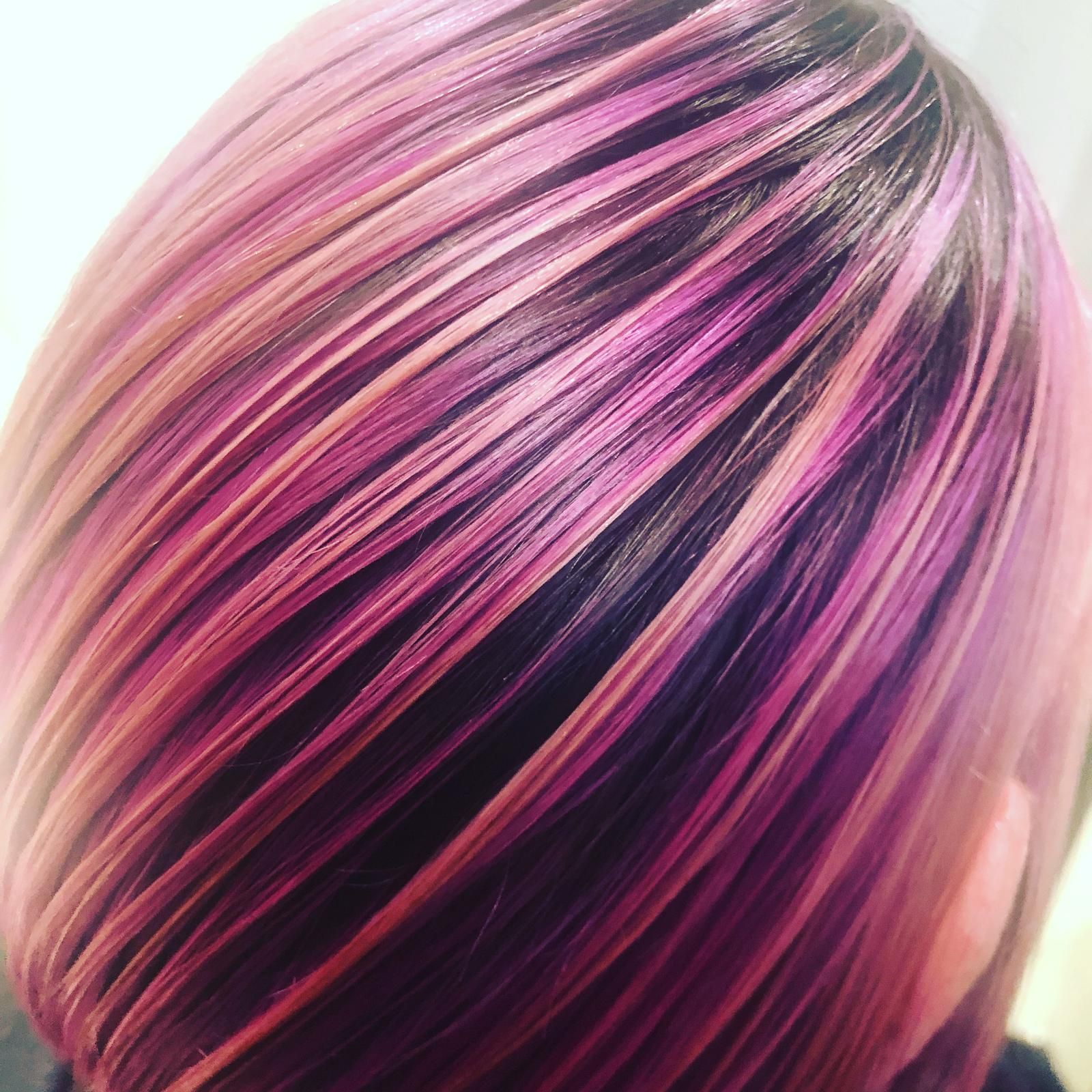 Close-up of hair with pink, purple, black, and blonde streaks in a glossy layered style