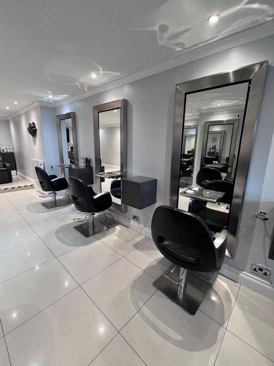 Modern hair salon with black styling chairs, mirrors, and glossy white floors