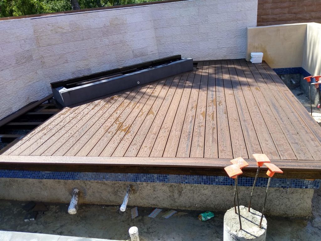 Brown deck under construction next to a wall. Gray planters and concrete pillars visible.