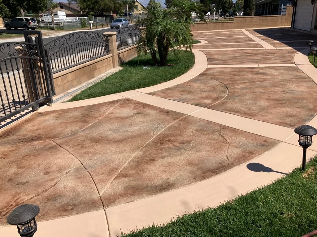 Driveway with decorative concrete in shades of brown, bordered by grass and a wrought iron gate.