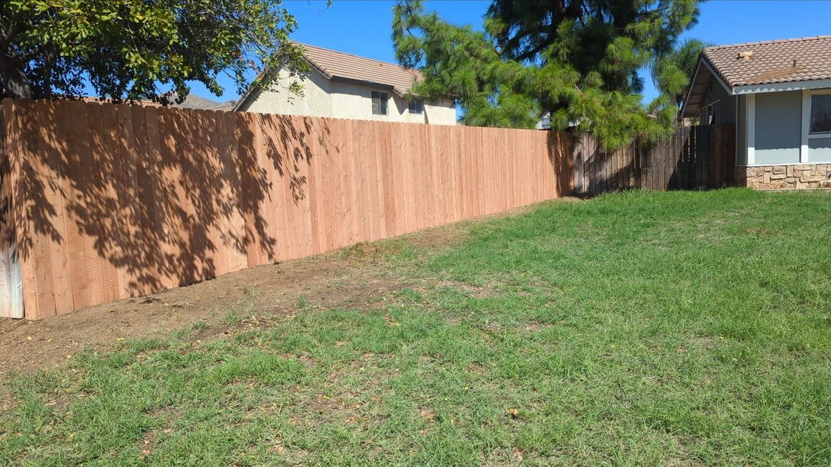 Brown wooden fence along green grassy yard with homes in the background.