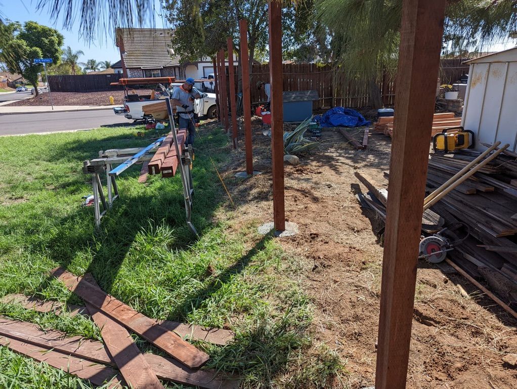 A person builds a fence with wooden posts in a yard.
