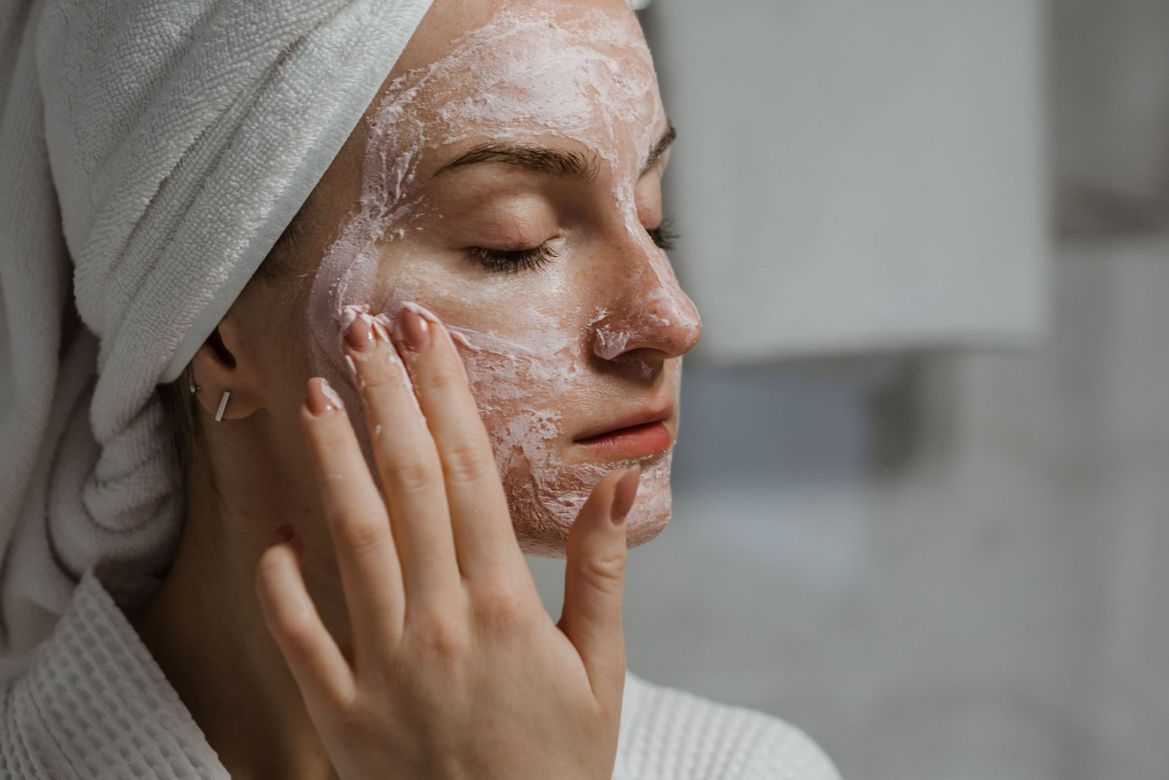 Woman applying facial skincare cream with a towel wrapped around her head.