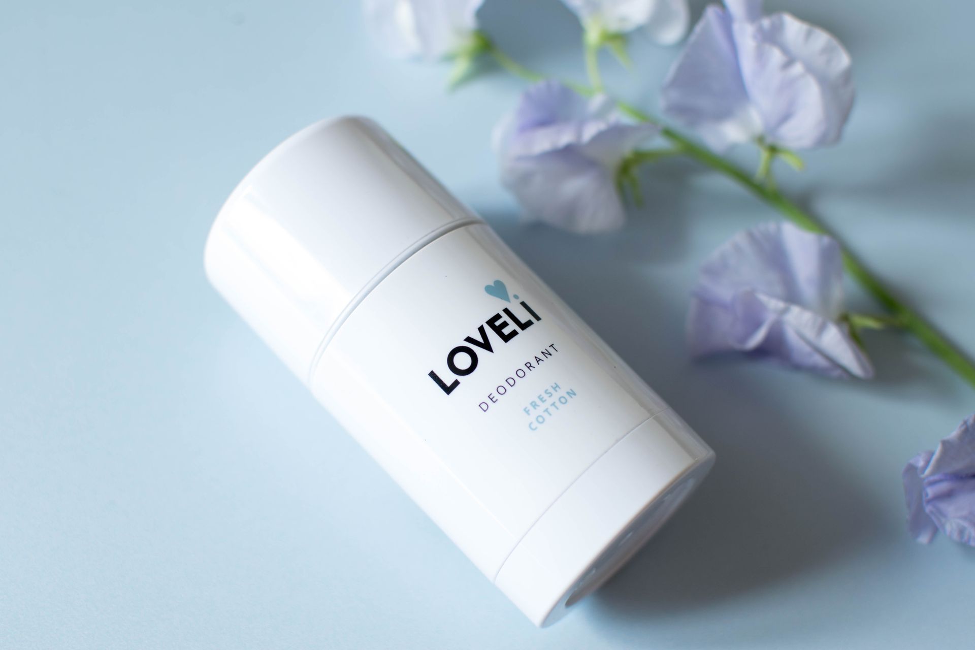 Een fles loveli deodorant staat op een blauw oppervlak
