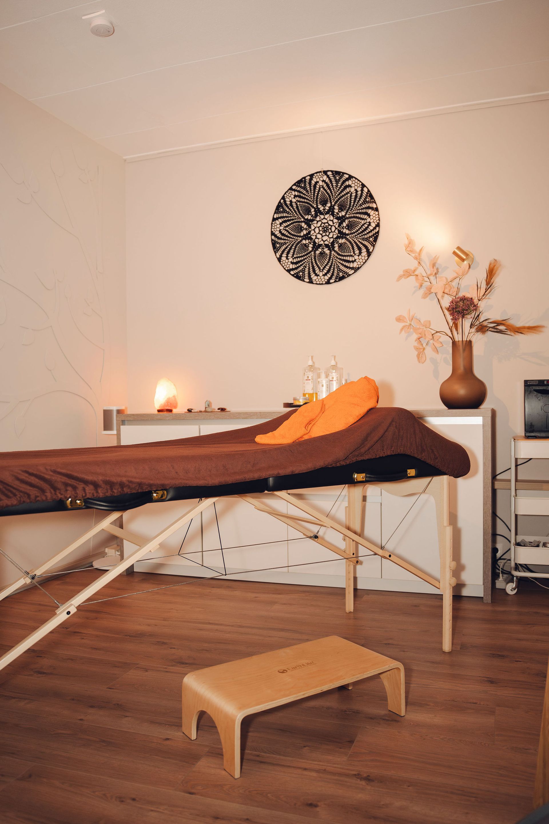 Een massagetafel in een kamer met een vaas met bloemen aan de muur.