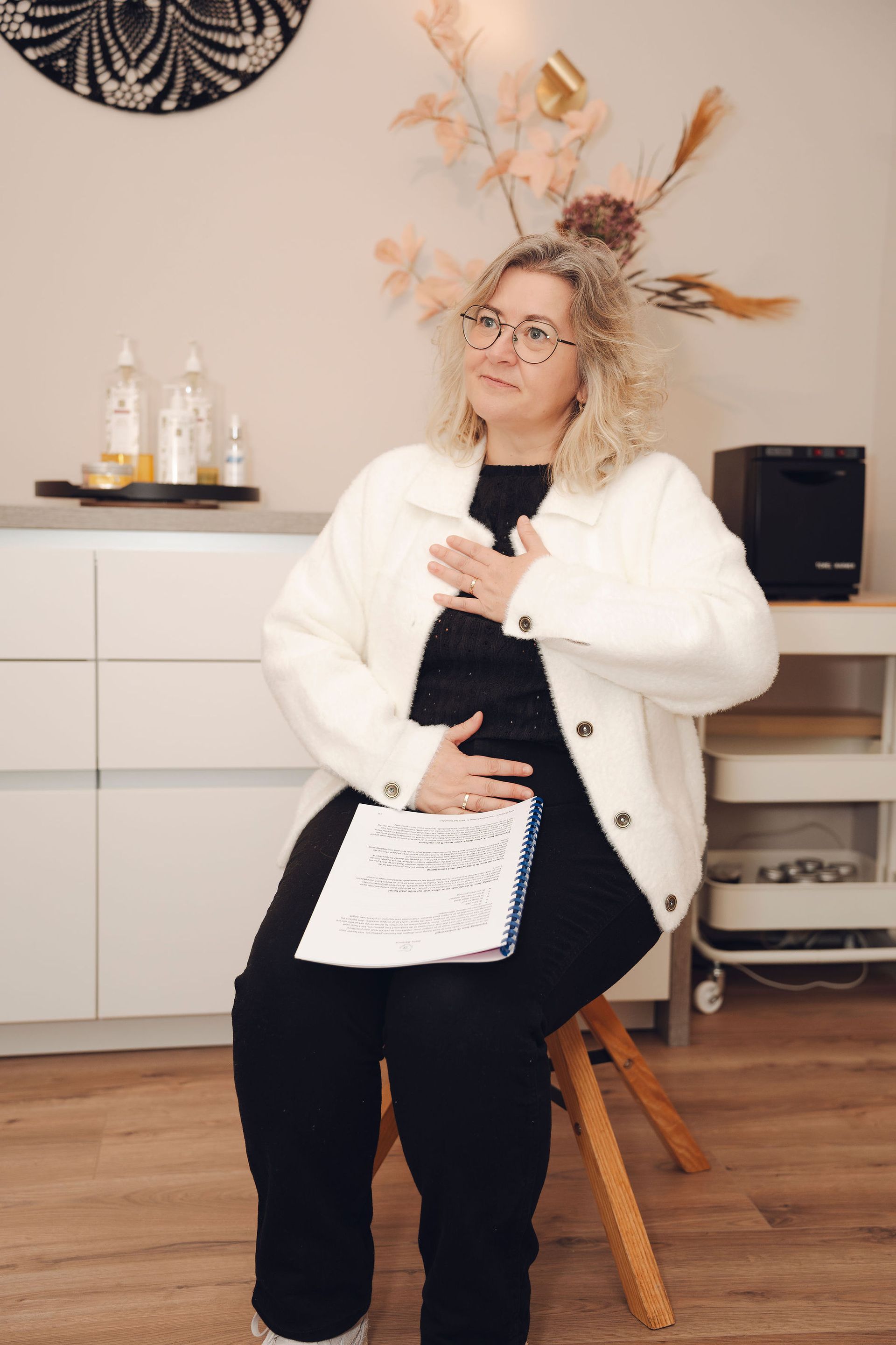 Een vrouw zit op een stoel met haar handen op haar borst.