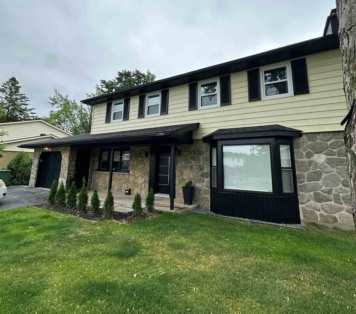 Two-story stone and beige house with black-trim windows and a green lawn in front