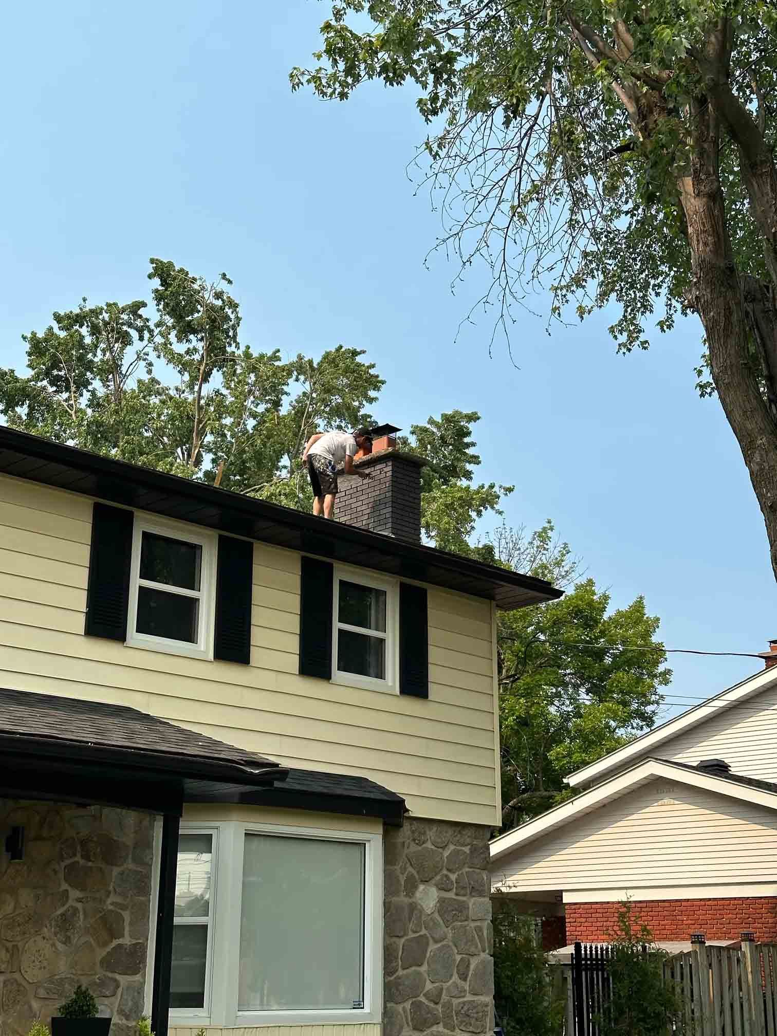 Two-story house exterior with stone and cream siding, black shutters, and trees overhead
