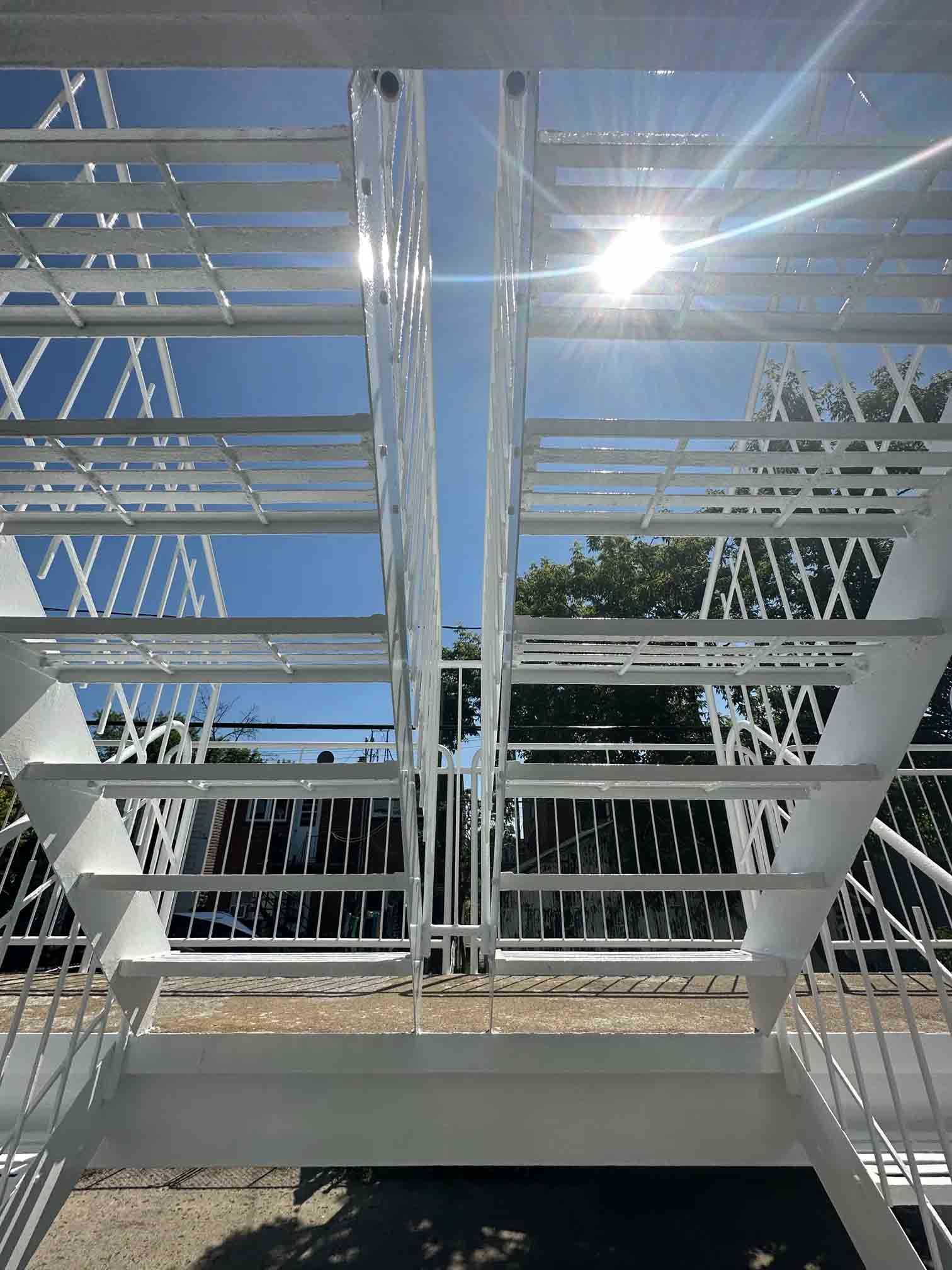 White metal staircase and railing under a bright blue sky, viewed from below.