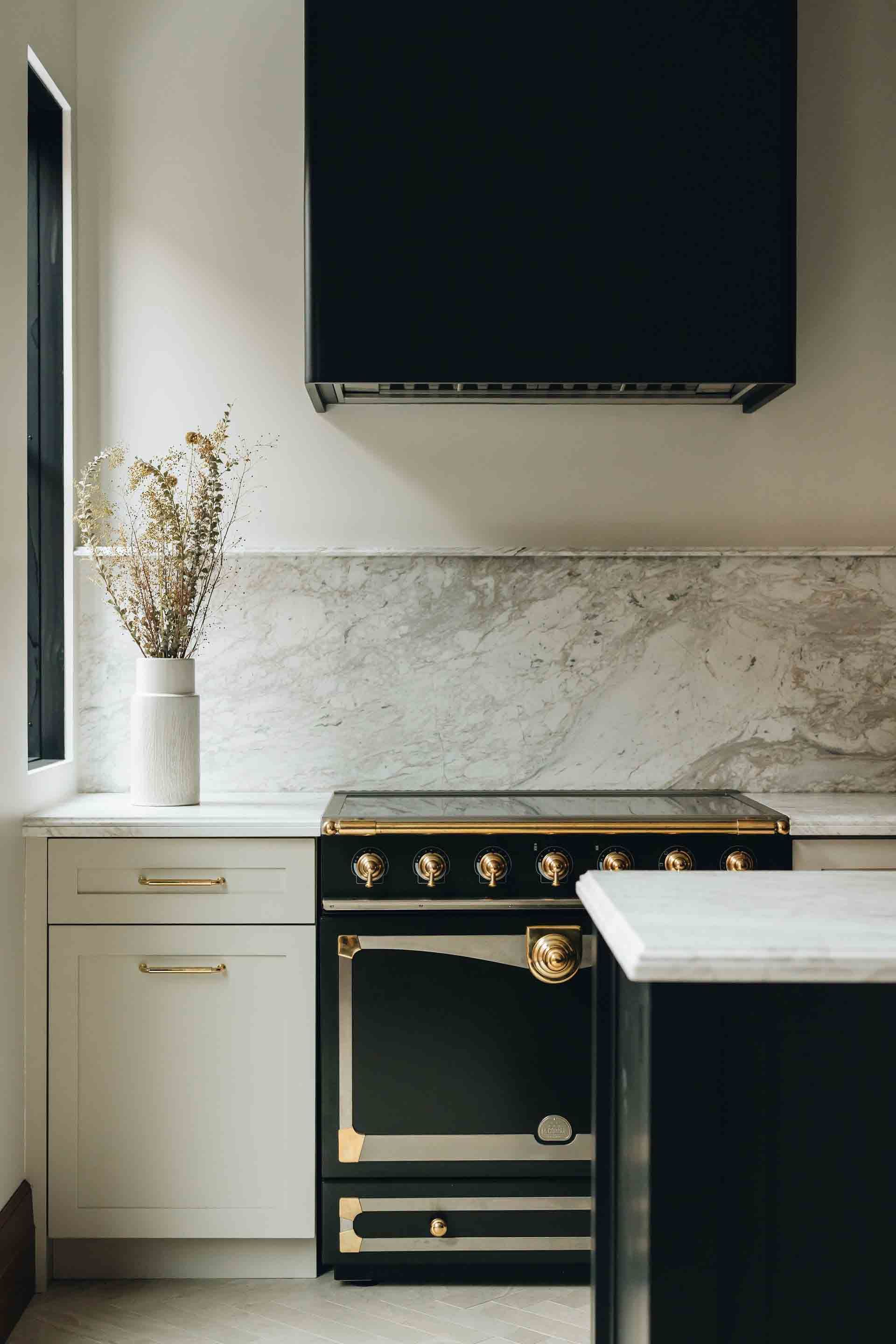 Modern kitchen with black stove, white cabinets, marble backsplash, and a vase of dried flowers
