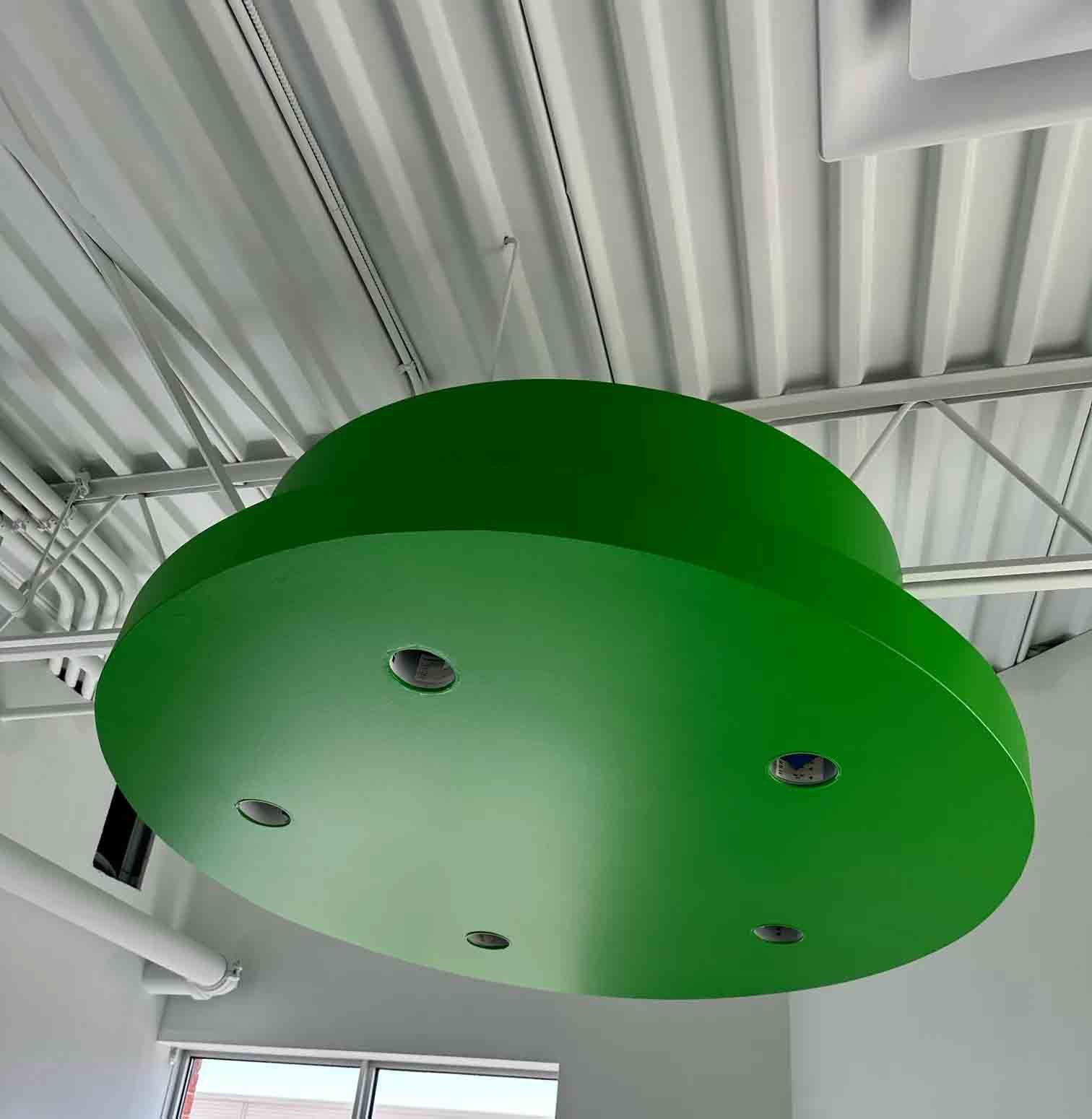 Bright green circular ceiling fixture with recessed lights on an industrial ceiling