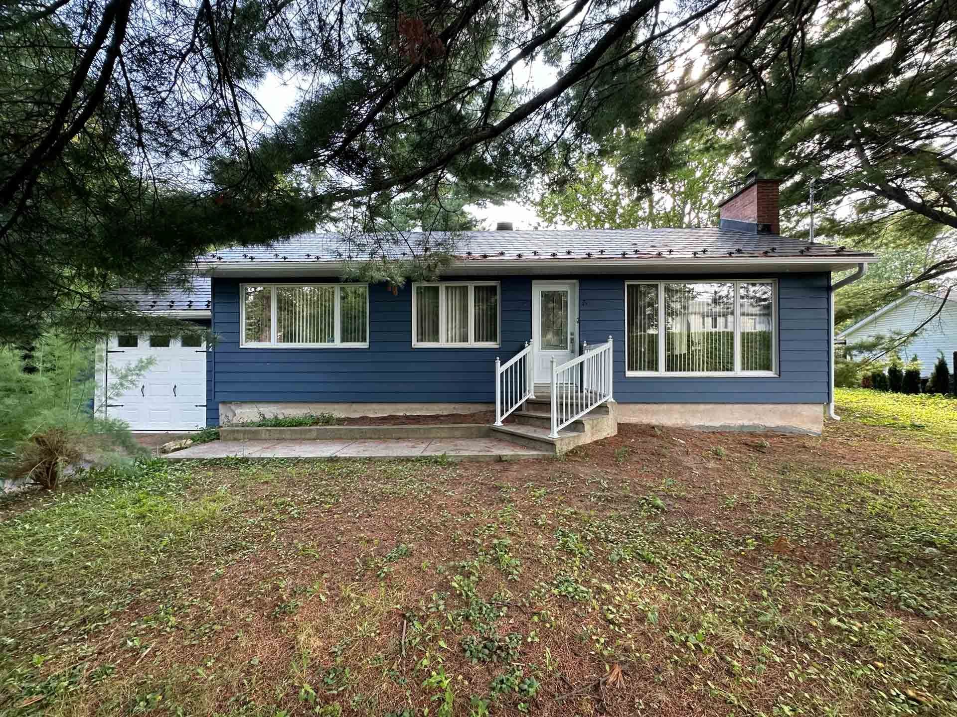 Blue single-story house with front steps, white trim, garage, and large tree in front yard