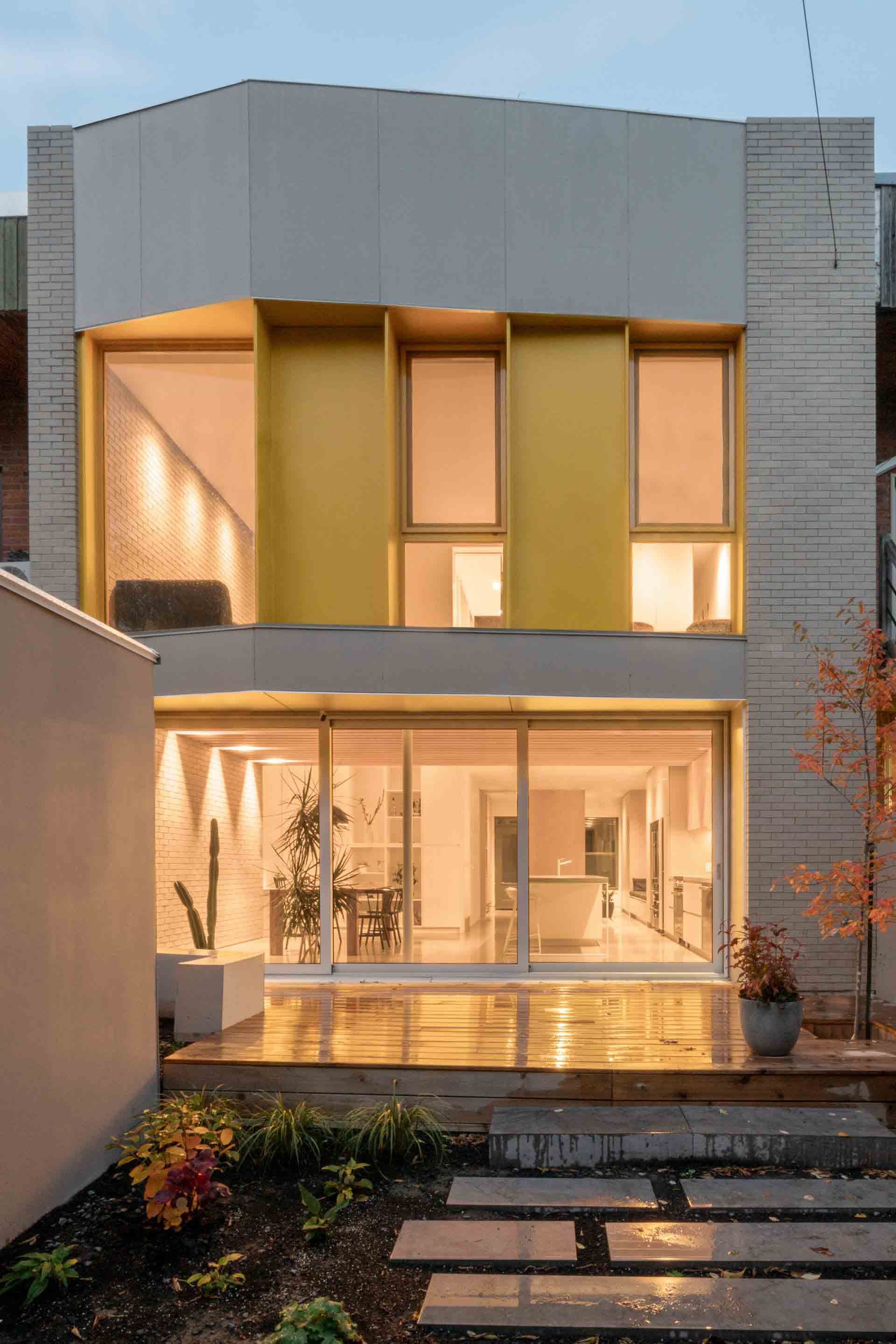 Modern two-story house with warm lit windows and a front walkway at dusk