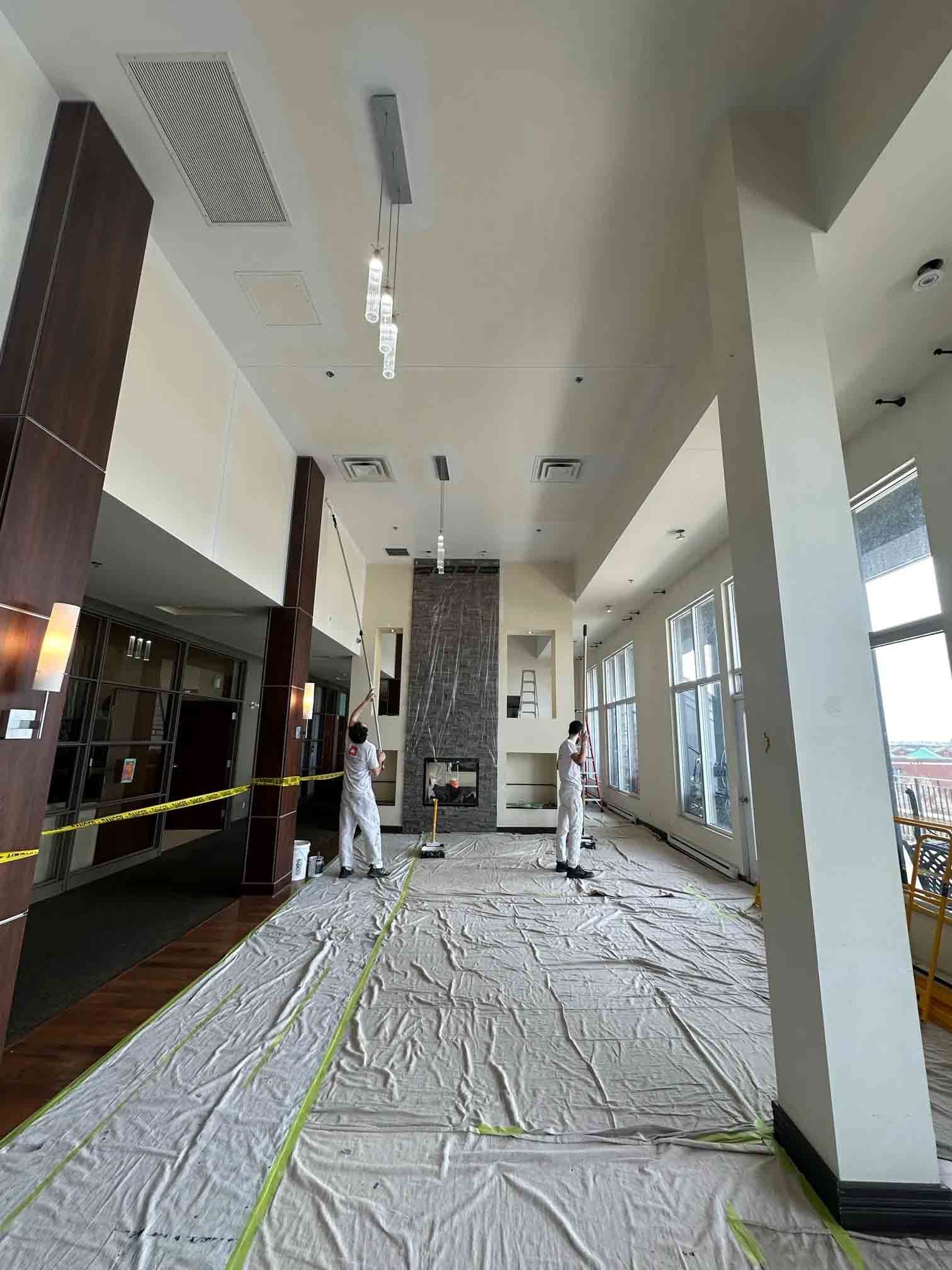 Hallway under renovation with protective floor covering, workers, and taped-off areas under bright ceiling lights