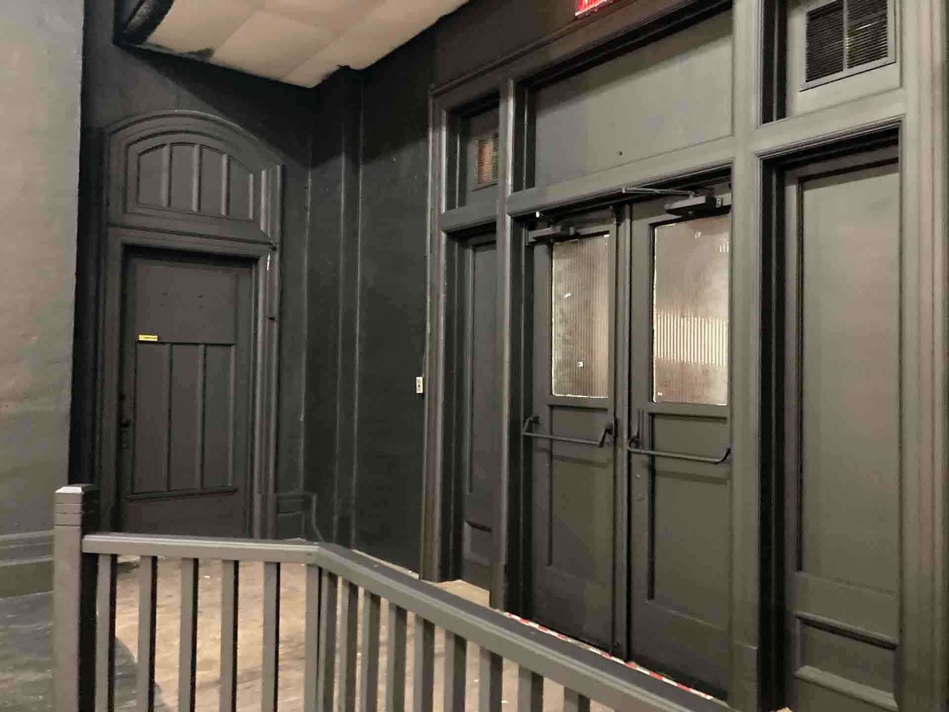Black storefront entrance with double glass doors, dark paneling, and a white railing in front