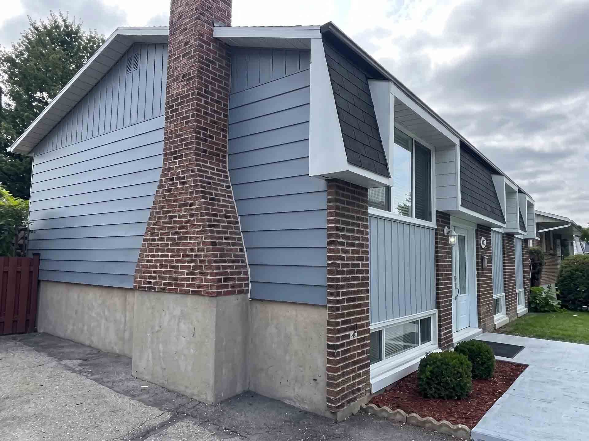 Row of gray townhouses with brick chimneys and white trim along a paved sidewalk