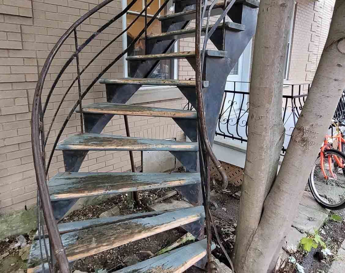 Rusty outdoor spiral staircase beside a brick building, with a bicycle visible in the background.