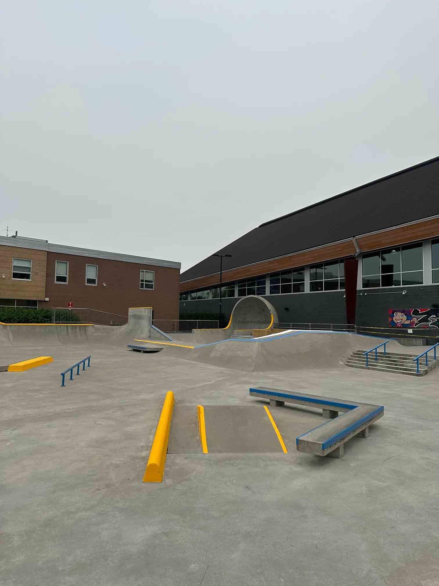 Outdoor school playground with ramps and rails on a concrete court beside brick buildings.