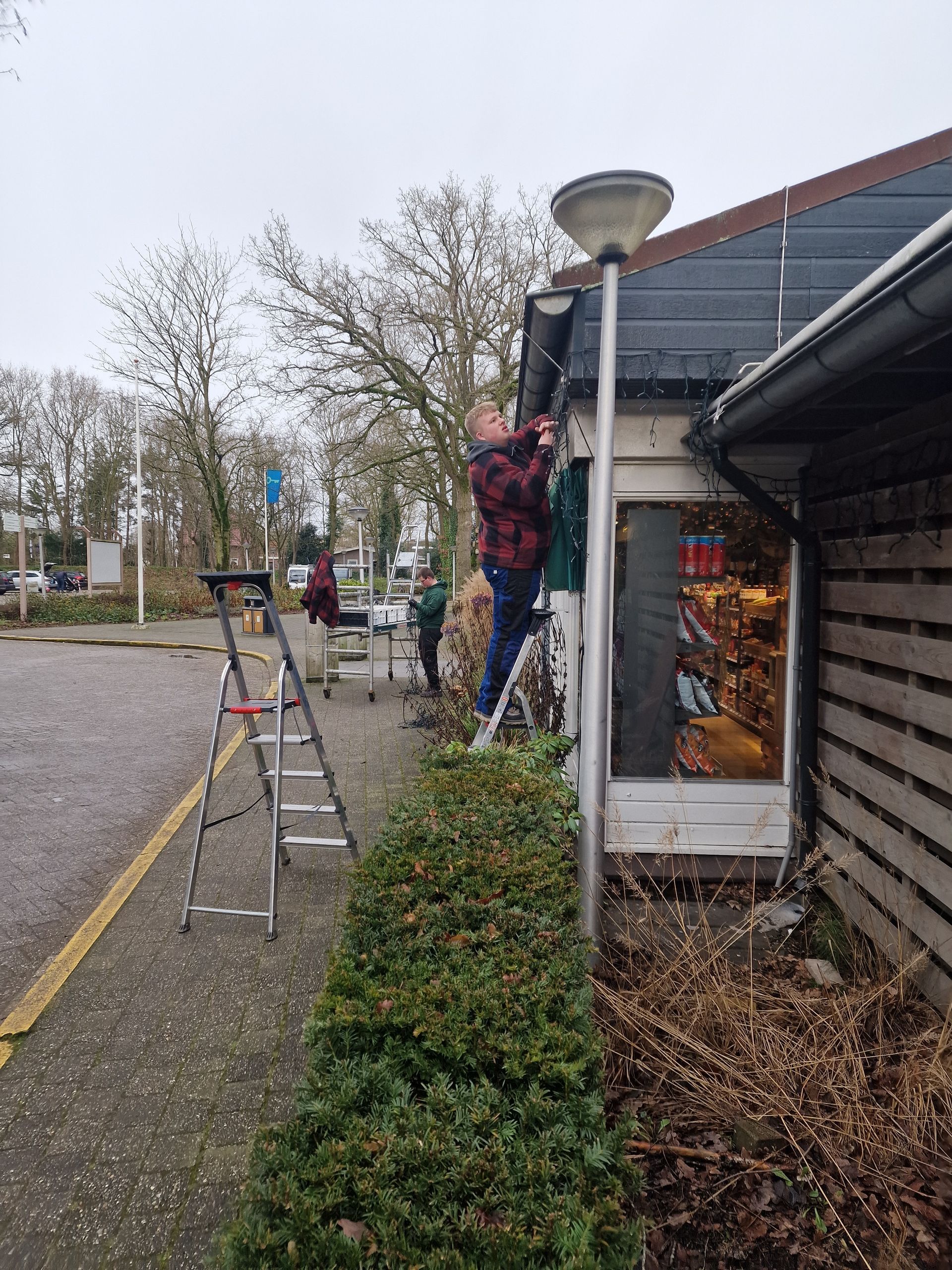 Een persoon op een ladder versiert de buitenkant van een gebouw met kerstverlichting.