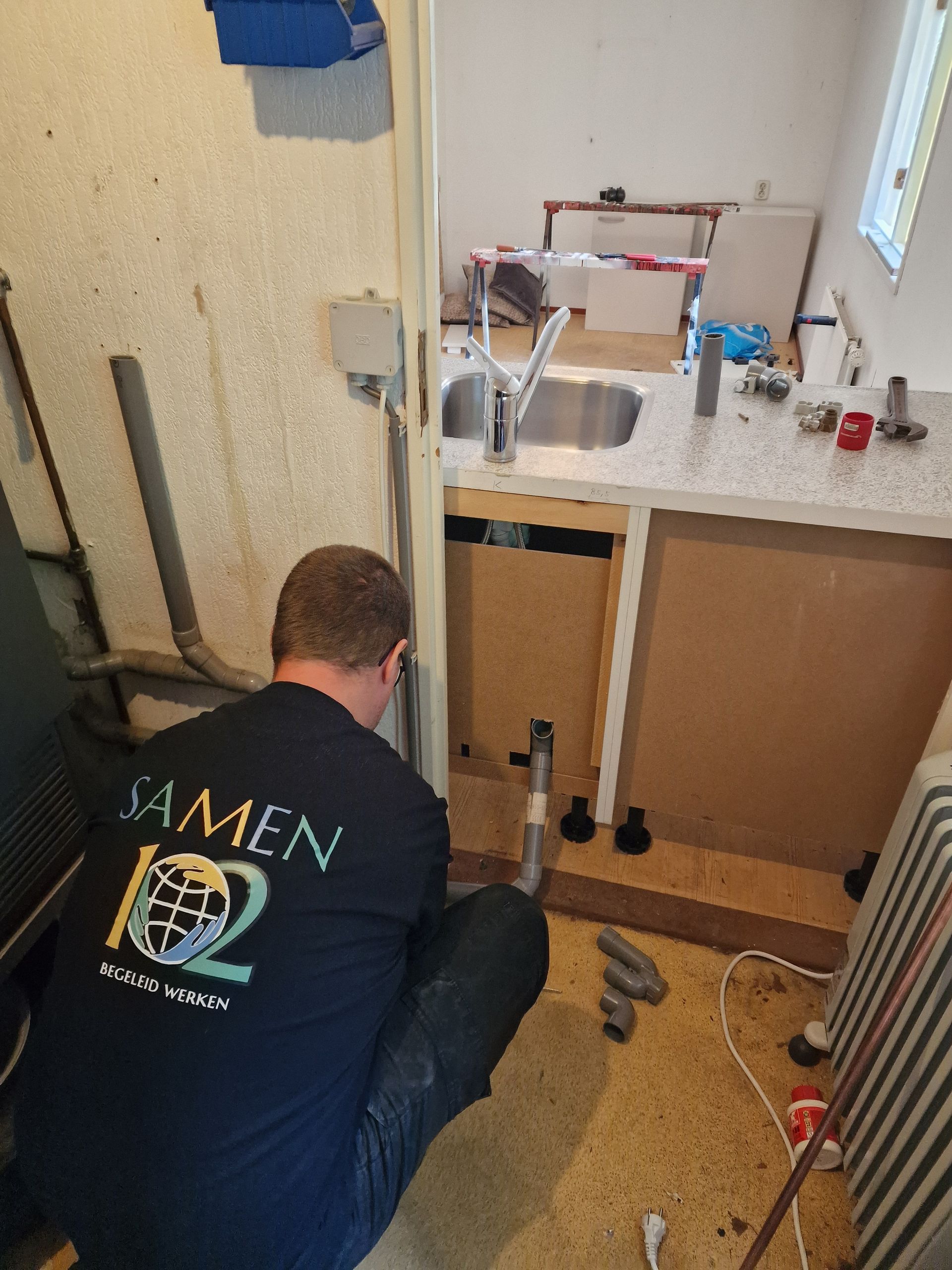 Man installeert keukenspoelbak in onafgewerkte ruimte.