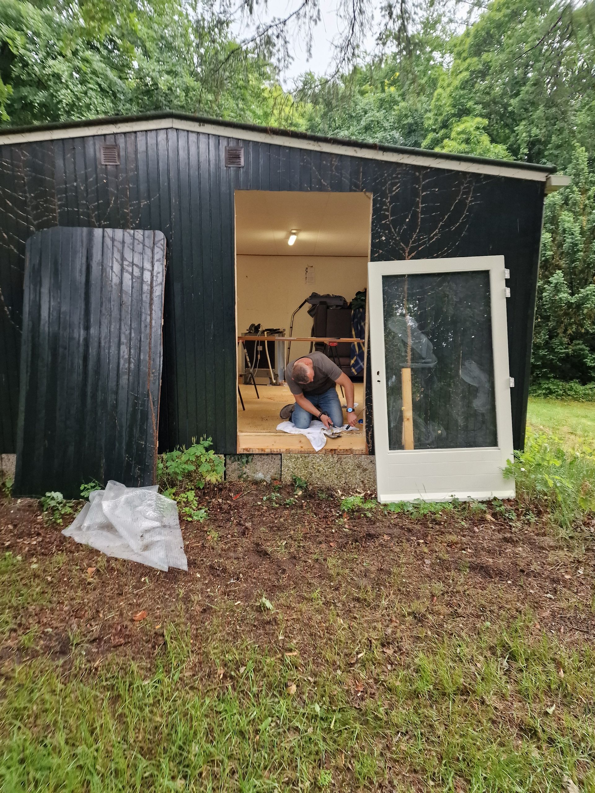 Een man is aan het werk in de schuur; aan de buitenkant van de schuur zijn een muur en een deur verwijderd.