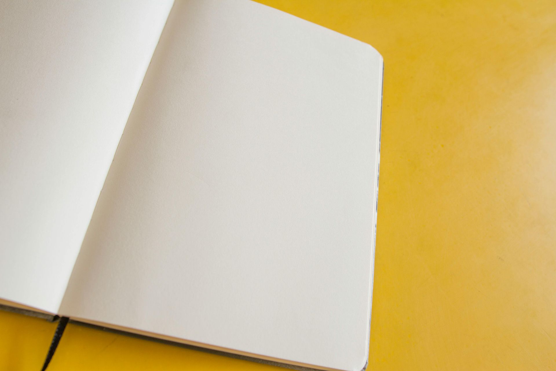 Een open notitieboek met blanco, witte pagina's op een gele ondergrond.