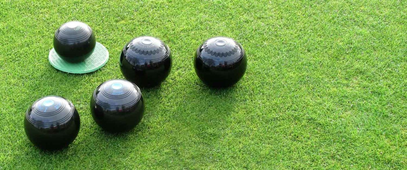 Five black bowls on green grass, one on a green disc.