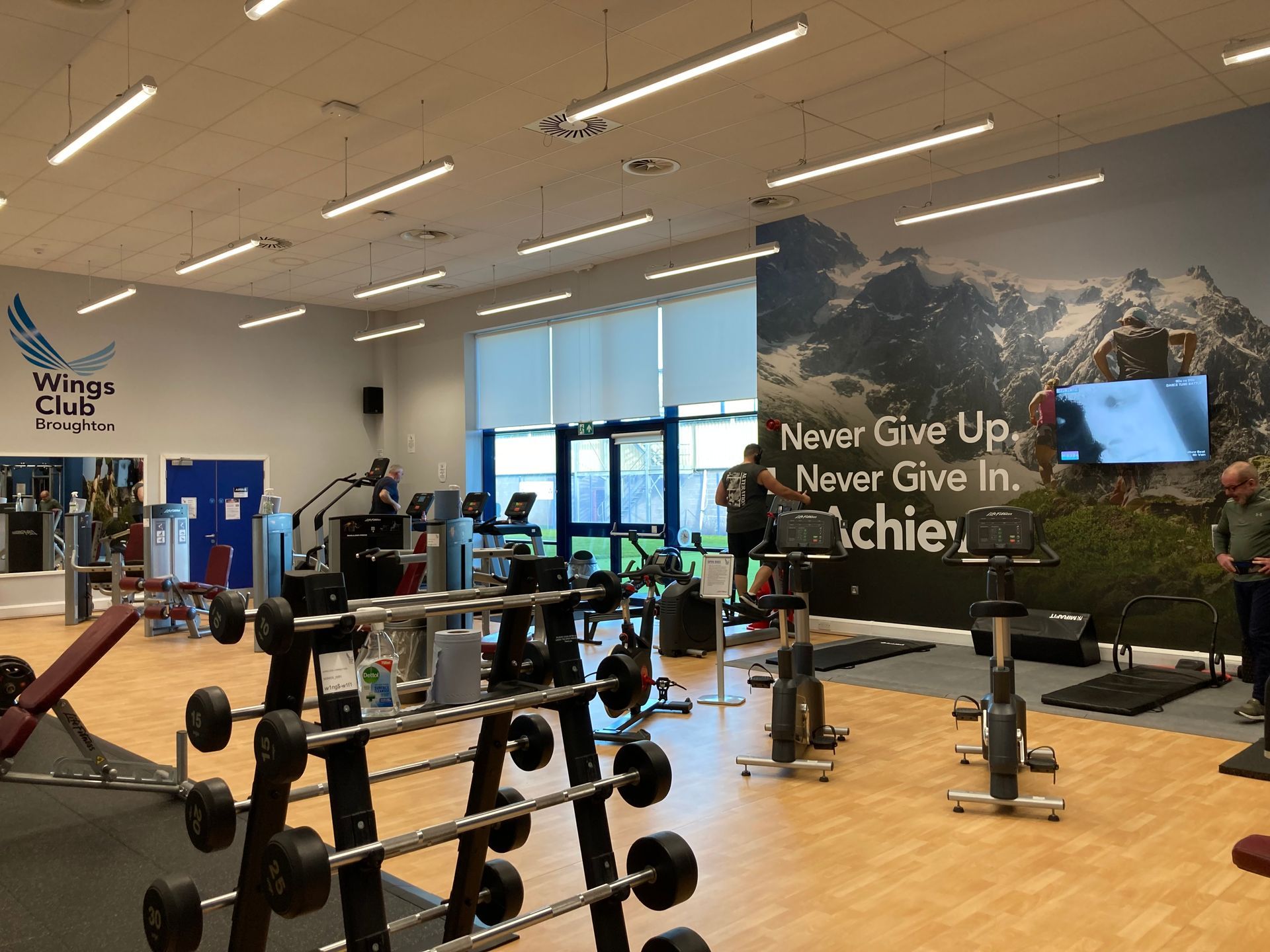 Gym interior with weight racks, exercise machines, and people working out. Wall mural with motivational quote.