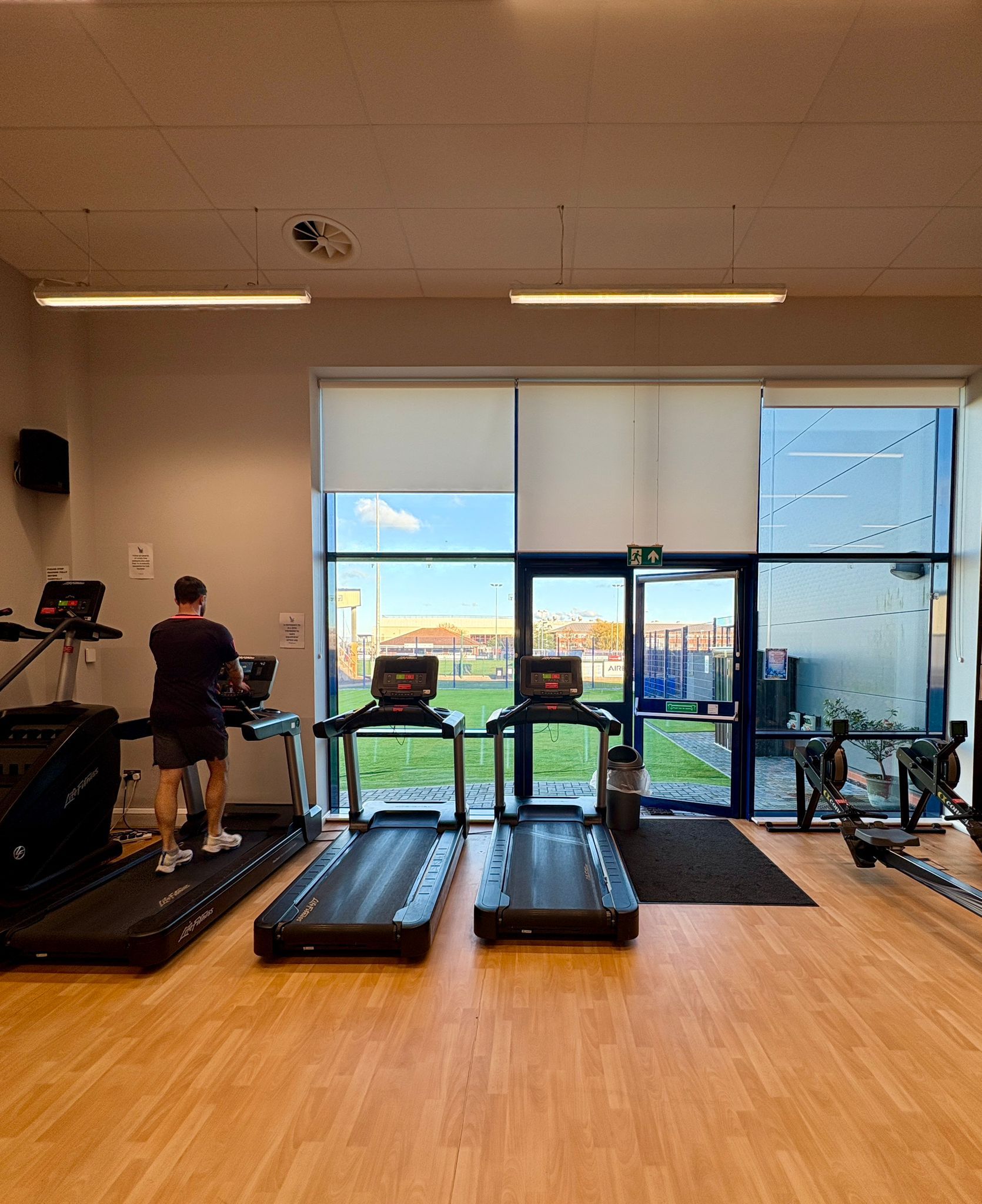 Man on treadmill in gym, windows with a view, treadmills, rowing machine.