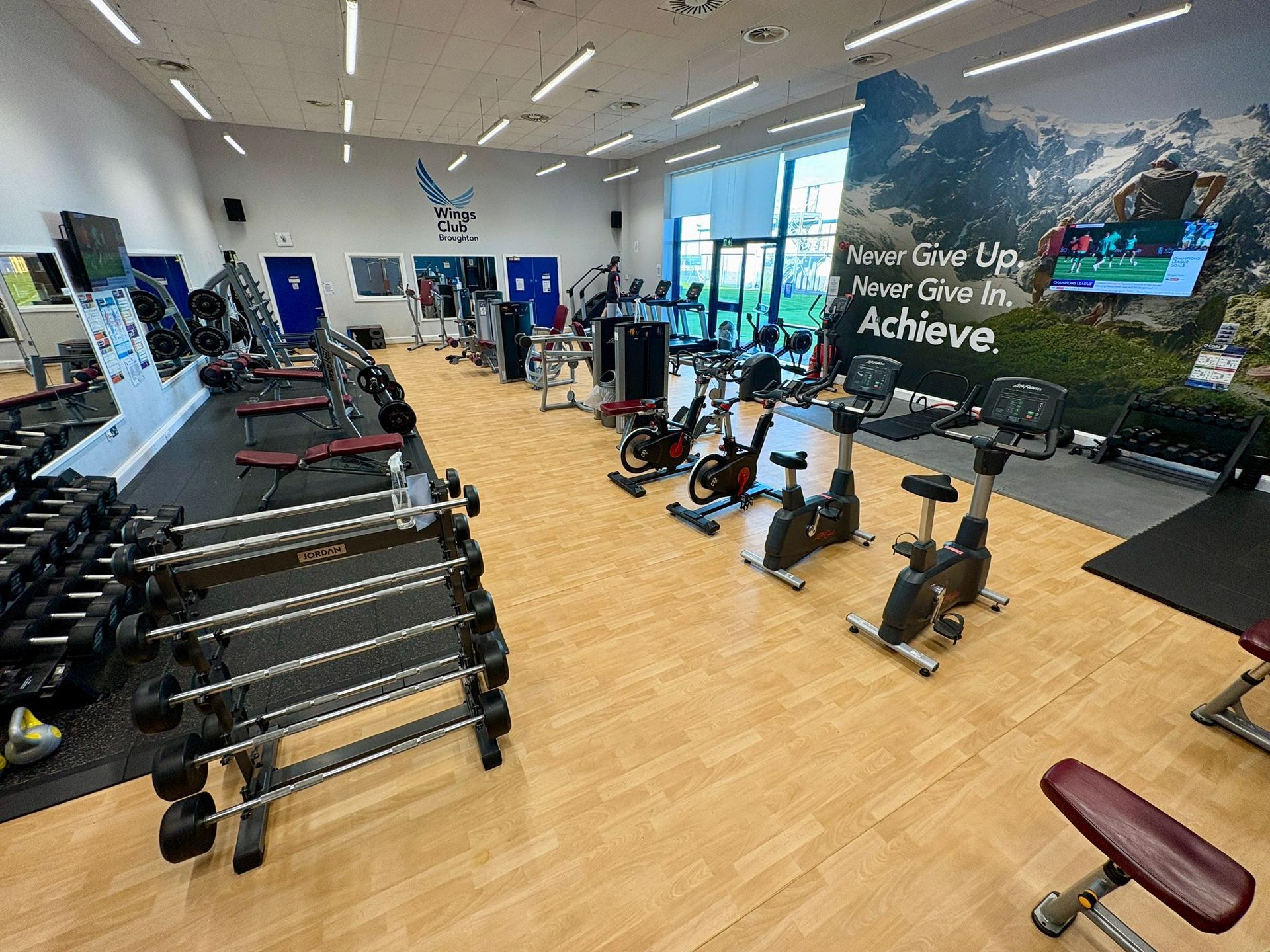 Gym interior with weights, cardio machines, and large motivational mural.