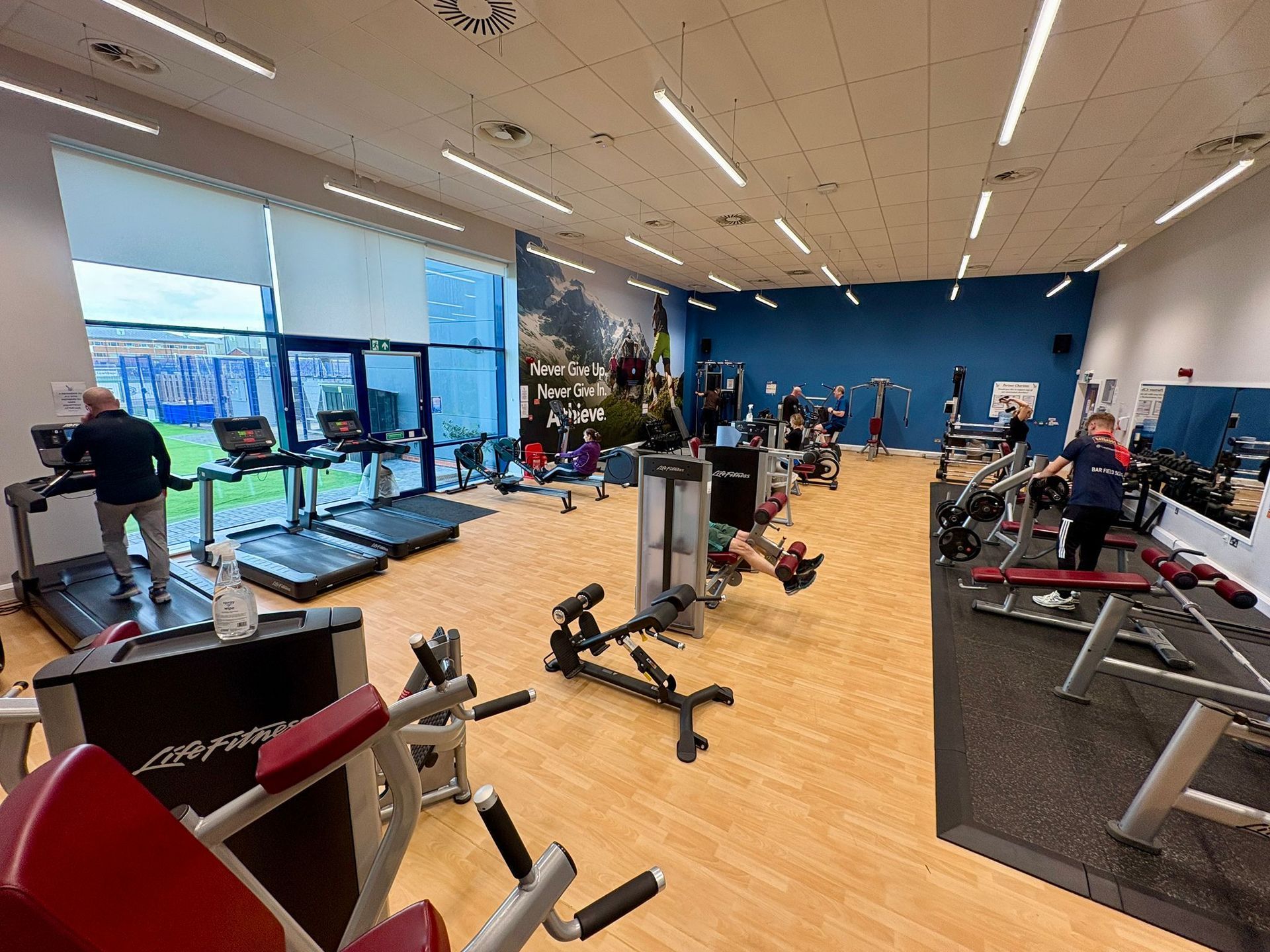 Gym interior with various exercise machines and people working out. Bright, modern space with blue and white accents.