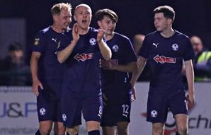 Soccer players in navy blue uniforms celebrate on a field at night.