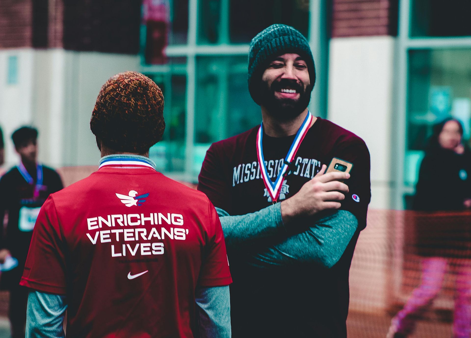Two men with medals smile. One wears a maroon shirt with