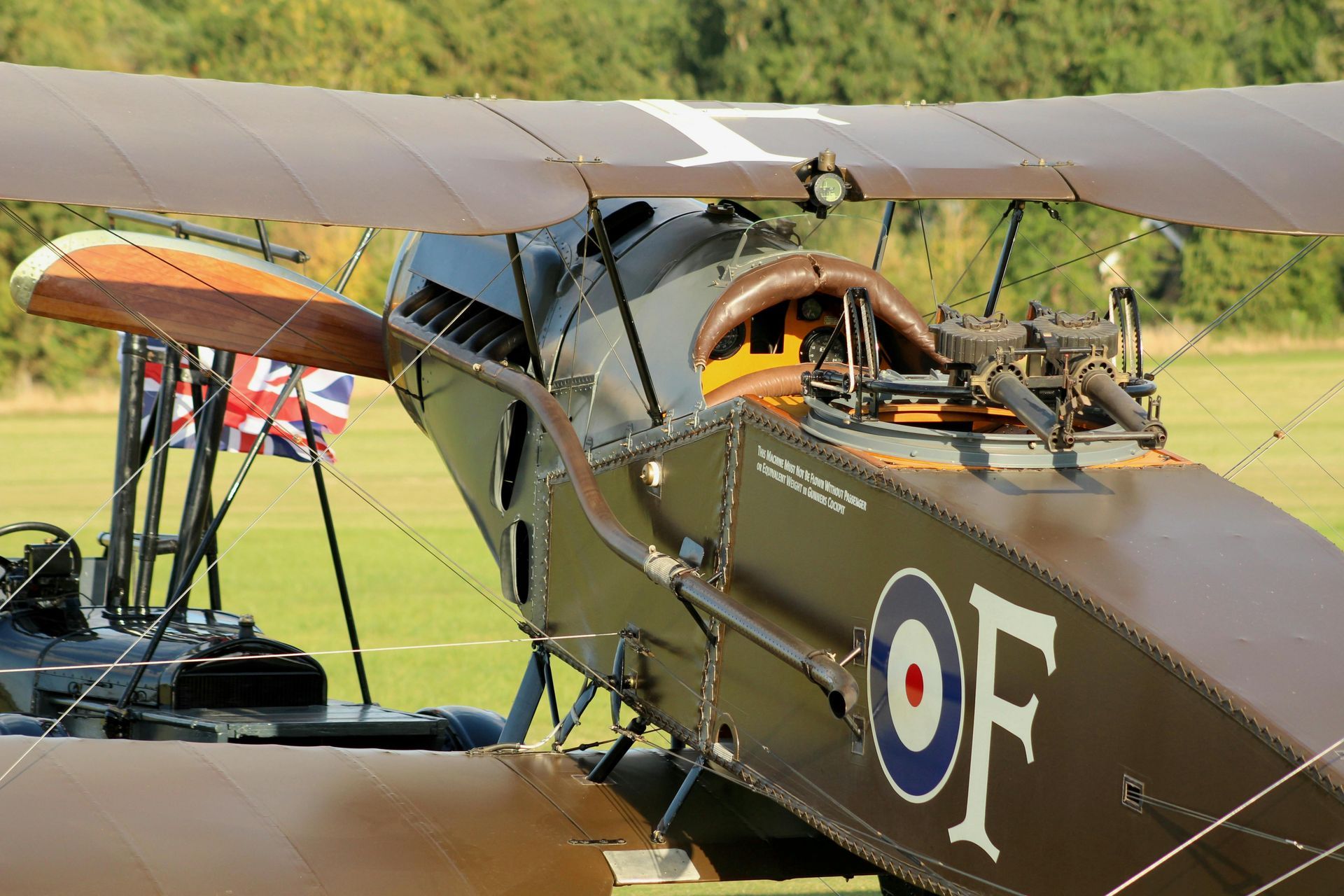 Brown biplane cockpit with wooden propeller and Union Jack flag in the background.