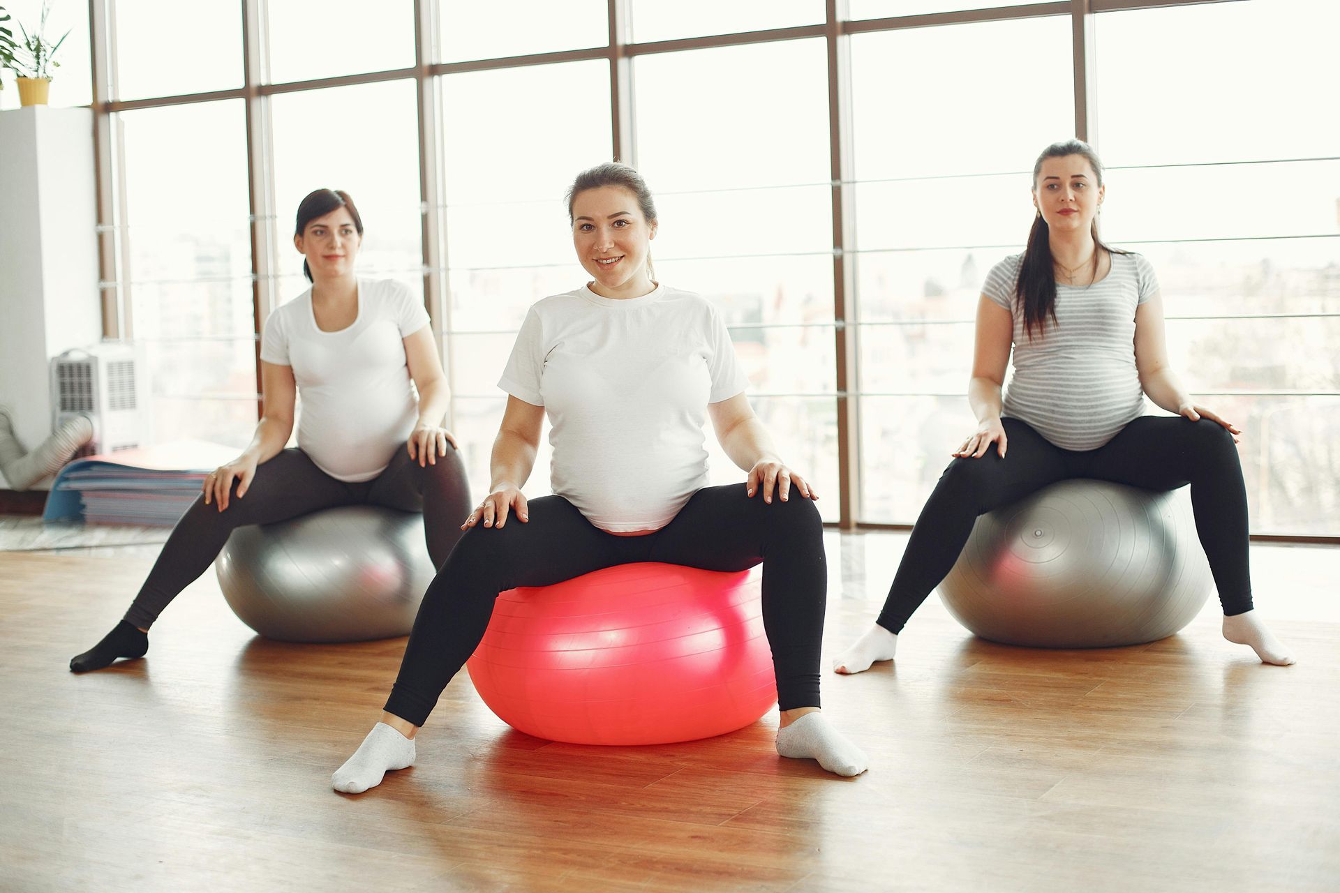 Three pregnant women exercising on fitness balls, indoors.