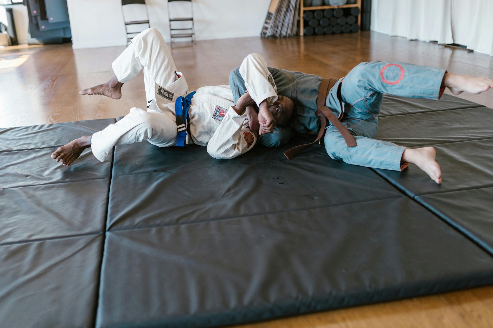 Two people in martial arts uniforms grappling on a mat. One is in a headlock.