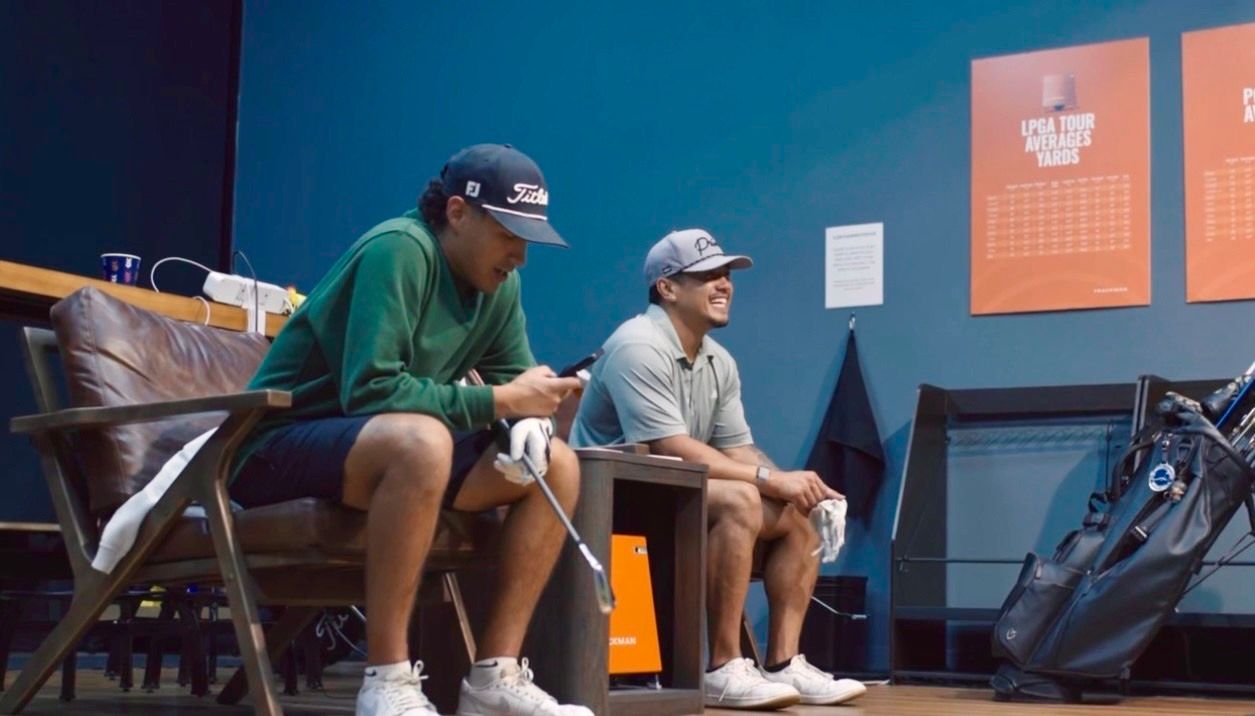 Two seated people waiting their turn on the Trackman golf simulator in Tulsa, OK.